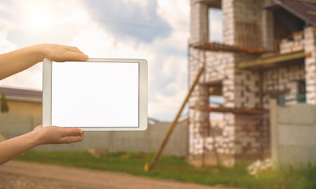 Building construction mockup, tablet with black white screen in hand on background of unfinished...