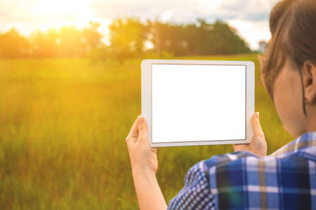 Planning for the building land, young girl holds tablet screen mockup next to field at sunset, nature background, copy space photoの写真素材