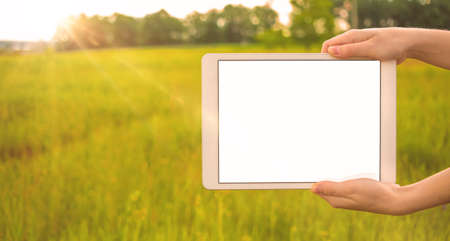 Hand with tablet screen mockup, background of sunny field, copy spaceの写真素材