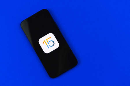 Kharkov, Ukraine - June 18, 2021: Apple iPhone 12 with iOS15 icon logo on the screen, blue office desktop top viewのeditorial素材