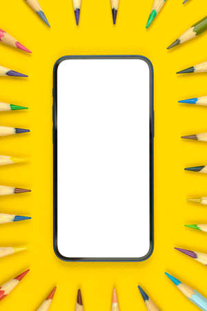 School flat lay workspace mockup with modern smartphone, copy space and blank white screen, yellow desktop with color pencils, top viewの写真素材