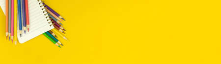 Back to school banner composition with notepad and color drawing pencils, yellow desktop table background, top view with copy spaceの写真素材