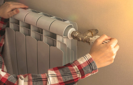 Close-up of woman hand on thermostatic valve of radiator heater in apartment