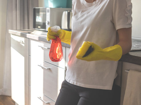Cleaning with spray detergent, female young woman in rubber gloves on kitchen in modern apartment...