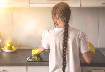 Young caucasian girl cleaning and polish electric cooker in kitchen, table top in the modern kitchenの写真素材
