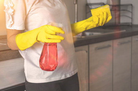 Female janitor cleaning kitchen, hand in the yellow gloves with spray and sponge
