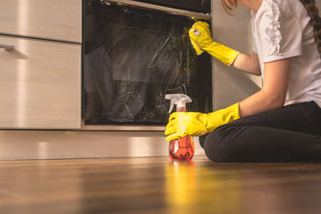 Woman use spray detergent to cleaning the kitchen oven sitting on the wooden floorの写真素材