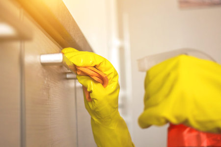 Woman cleaning the kitchen and kitchen cabinet in yellow rubber glove and dish cloth wuth spray...