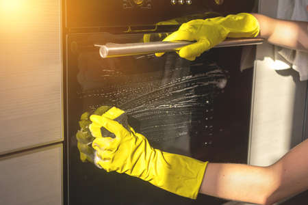 Washing electric oven in modern kitchen, yellow rubber gloves and sponge in the handの写真素材