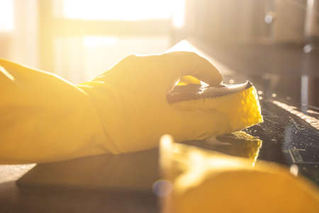 Housework after work concept, hand in yellow glove with sponge, sunset, kitchen cleaning backroundの写真素材