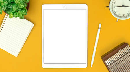 Top view of creative designer workspace with digital tablet mockup and office supplies on white desk, notepad, alarm clock and stylus pen, copy spaceの写真素材