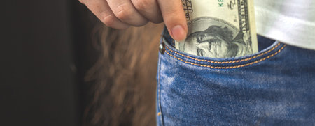 Dollars in pocket, banner. Young woman hand putting money banknote in her denim jeans pocket....