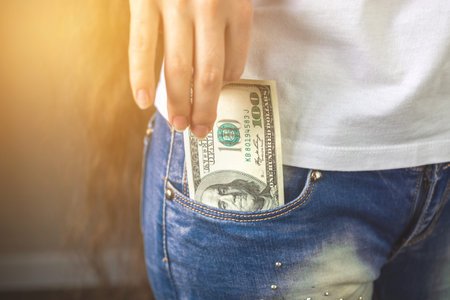 Dollars in pocket. Young woman hand putting money her denim jeans pocket. Concept photo of wealth