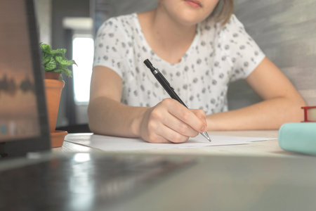 Young student girl holding pencil and writing. Education concept background. Wooden table with...