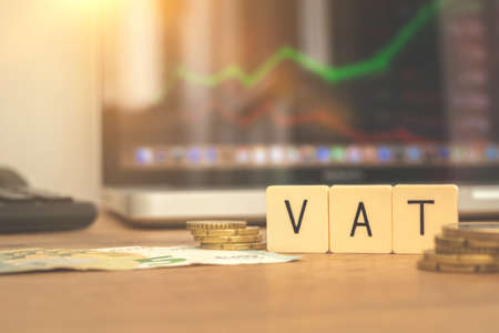 VAT concept. Word VAT and coins on stock market or forex trading graphs and candlestick background. Business and investmentの写真素材