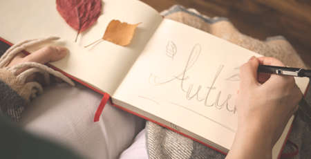 Banner female holding pencil and writing something in notebook. Fall season scene or hygge concept backgroundの写真素材