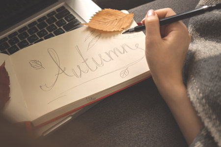 Diary with hand written word Autumn, cozy home concept. Hand with pencil and warm plaid on the sofa