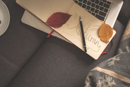 Hand written Autumn word in notepad, cozy home background. Pencil and autumn leaves on old paper, copy spaceの写真素材