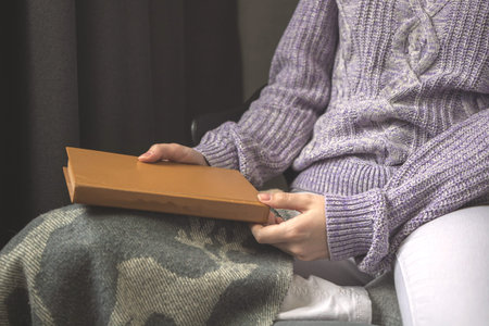 Senior woman holding old book, woman in woolen sweater and warm plaid on legs, concept photo of cold winter daysの写真素材