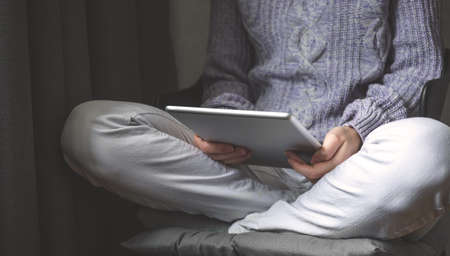 Reading concept. Young woman with tablet pc relaxing in cozy house, sitting on chair. Front view, selective focusの写真素材