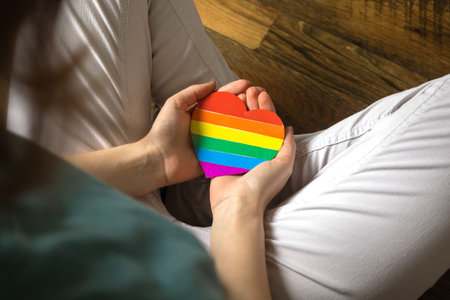 Caucasian lady holding rainbow color flag in heart shape, symbol of LGBT pride month celebrate,...