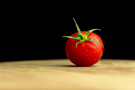 Small red cherry tomatoes on a wooden board on a black background with copy space photo