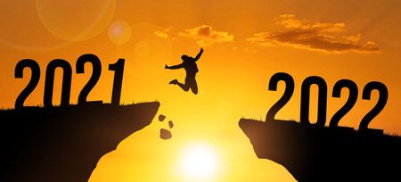 Silhouette man kumping between cliff 2021 to 2022 on sunset sky background. New Year card, banner...
