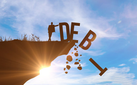 DEBT concept. Silhouette of man pushed off DEBT word from a cliff. Blue sky background. Success and profit conceptの写真素材