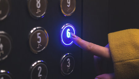 Woman hand pushing elevator button closeup view with led lights. Hand in yellow jacketの写真素材