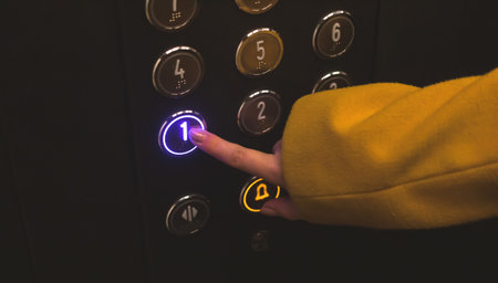 Woman press and pushing button first floor on elevator control panel. Hand close-up view photoの写真素材