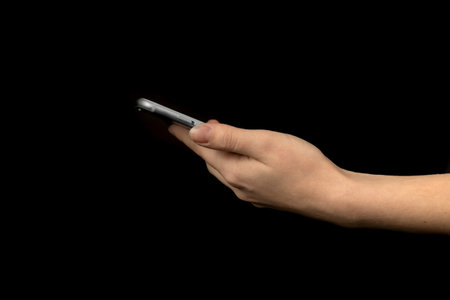 Close-up of hand using mobile phone against black background photoの写真素材