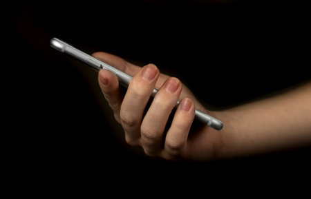 Female hand using smartphone on a black background photoの写真素材