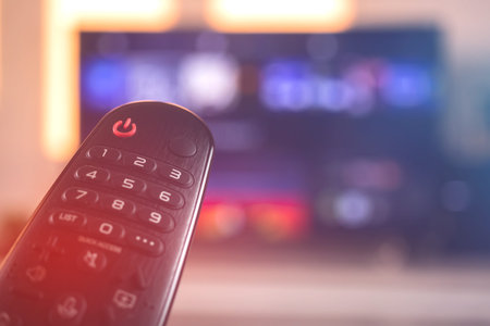 Smart TV remote control. Hand with TV remote control with a television on a background, closeup...