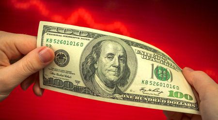 Dollar falls, US money on a red stock chart currency exchange rate background in businesswoman hands close-upの写真素材