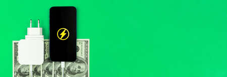 Green energy, saving energy concept. Mobile phone charger adapter and money on the table. Banner, green background with copy spaceの写真素材
