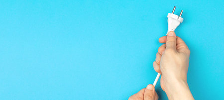 Hands holding power cable on a blue background, banner, flat lay, top view and copy space