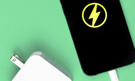 Smartphone charger adapter. Mobile phone with energy icon on the screen. Mint background, top view
