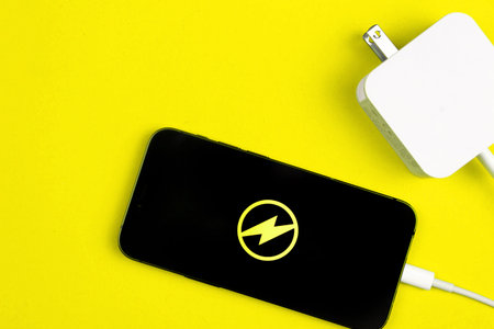 Smartphone charger adapter. Mobile phone with energy icon on the screen. Yellow background, top view