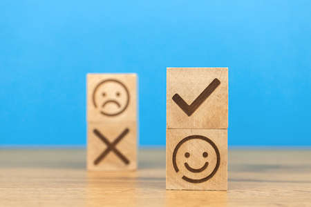 Customer choose positive smiley face and blurred sad face icon on a wooden cubes. Concept of service rating, satisfaction, business marketing backgroundの写真素材
