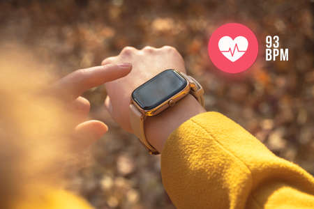 Smart watch with heart rate icon, healthcare concept. Woman measuring heart rate outdoorsの写真素材