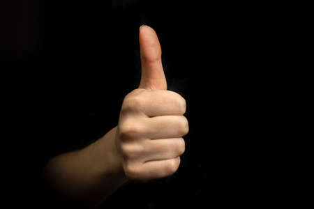 Success gesture, hand with thumb up sign on a black background, business conceptの写真素材