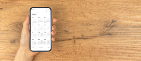 Calendar for 2022 on smartphone screen. Wooden background, banner. New year planning conceptの写真素材
