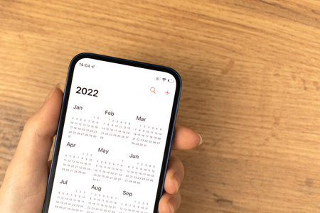 Calendar for 2022 on smartphone screen, close-up view. Wooden background. New year planning conceptの写真素材