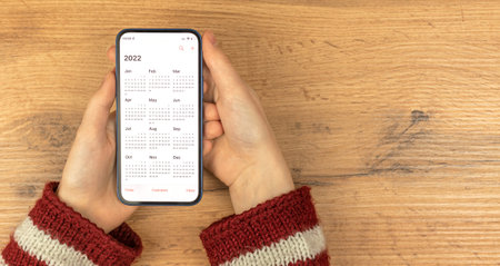 Calendar for 2022. Smartphone in woman hands. Wooden background. New year planning conceptの写真素材