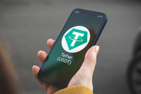 Tether USDT cryptocurrency symbol, logo. Business and financial concept. Hand with smartphone, screen with crypto icon closeupの写真素材