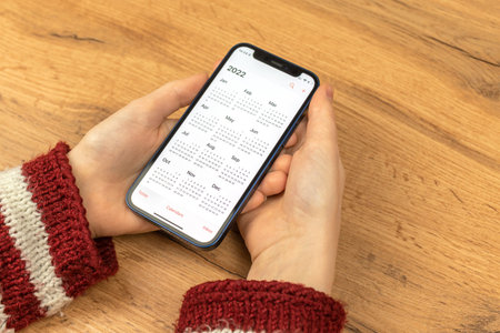 Kharkov, Ukraine - November 17, 2021: Woman open Calendar 2022 app on the Apple iPhone screen. Wooden backgroundのeditorial素材