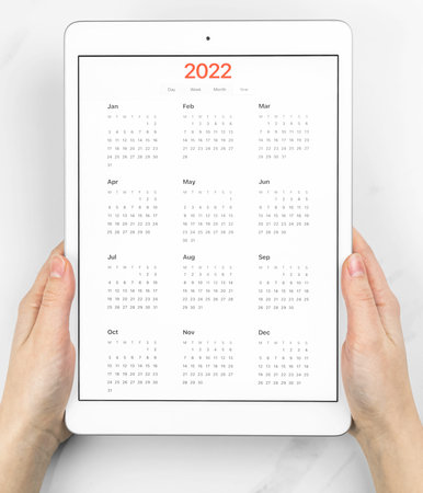 2022 calendar on screen, hands with tablet computer. White marble background. Concept of planning...