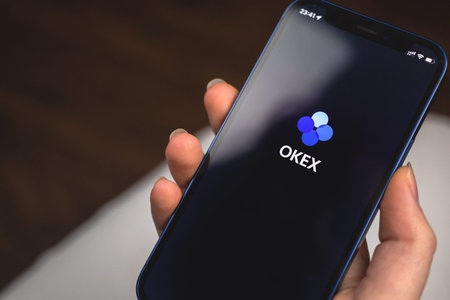 Kharkov, Ukraine - January 10, 2022: Woman uses OKEx Crypto app. Hand with Apple iPhone 12, mobile...