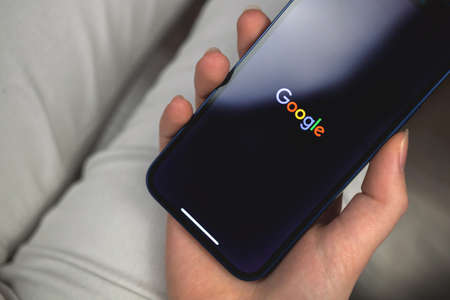 Kharkov, Ukraine - January 10, 2022: Woman uses Google app. Hand with Apple iPhone 12, mobile phone screen with logoのeditorial素材