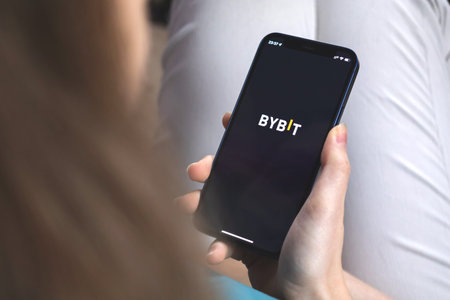 Kharkov, Ukraine - January 10, 2022: Woman uses Bybit app. Hand with Apple iPhone 12, mobile phone...